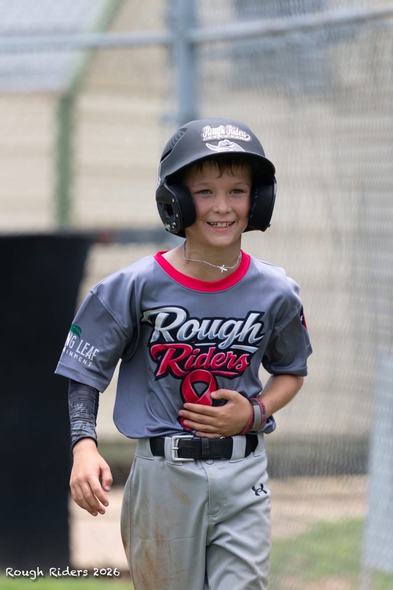 A smiling Rough Riders baseball player wearing his helmet