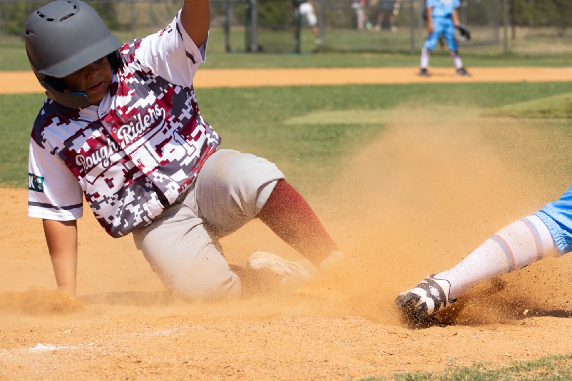 Rough Riders baseball player sliding through a cloud of dust
