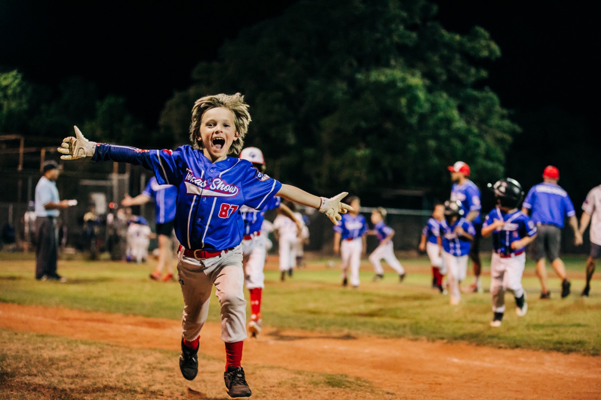 A young baseball player running toward the camera with his arms wide in celebration