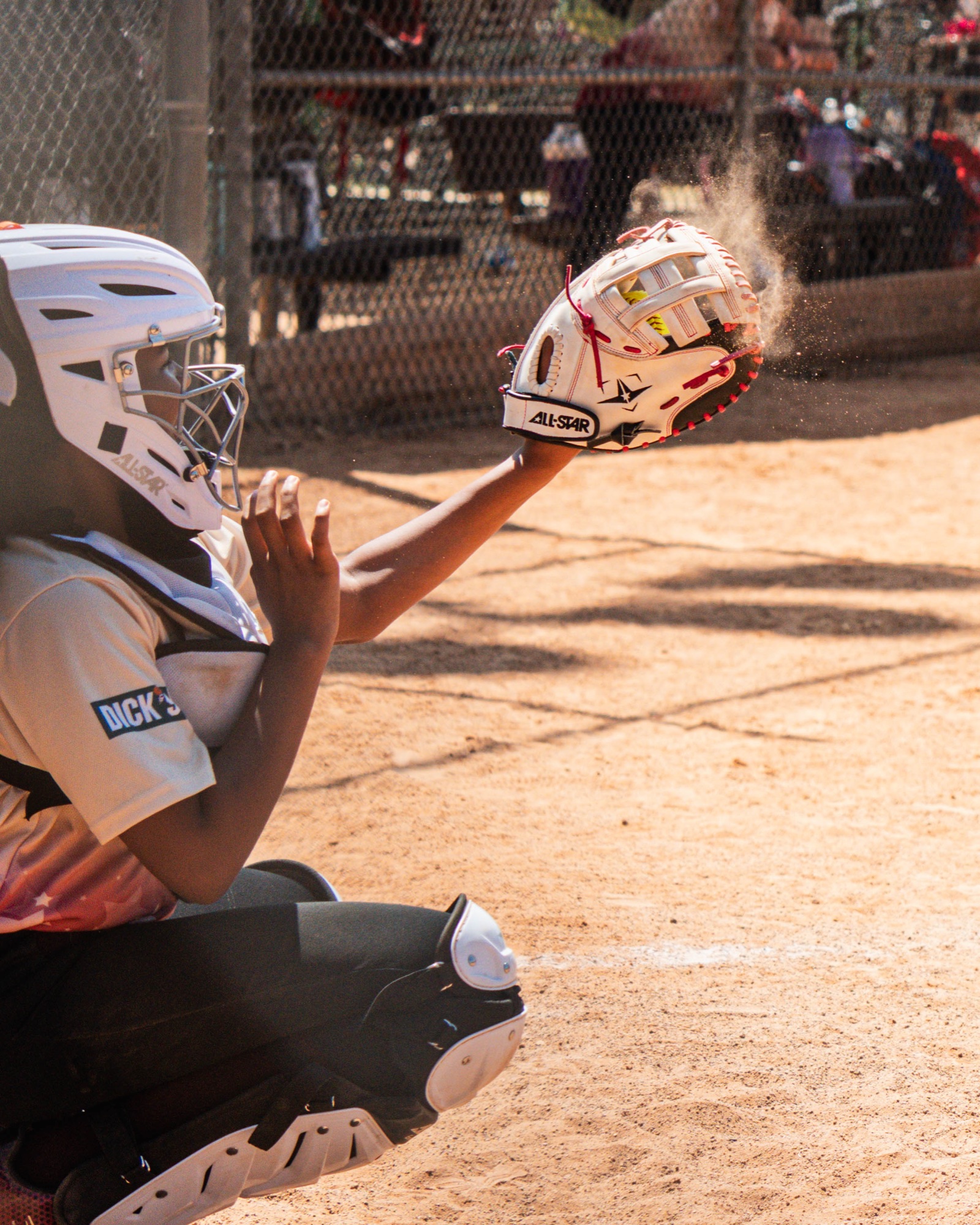 Rough Rider Youth softball catcher receiving a pitch through a cloud of dust