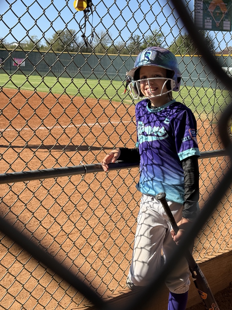A Rough Rider Youth softball player smiling beside the field